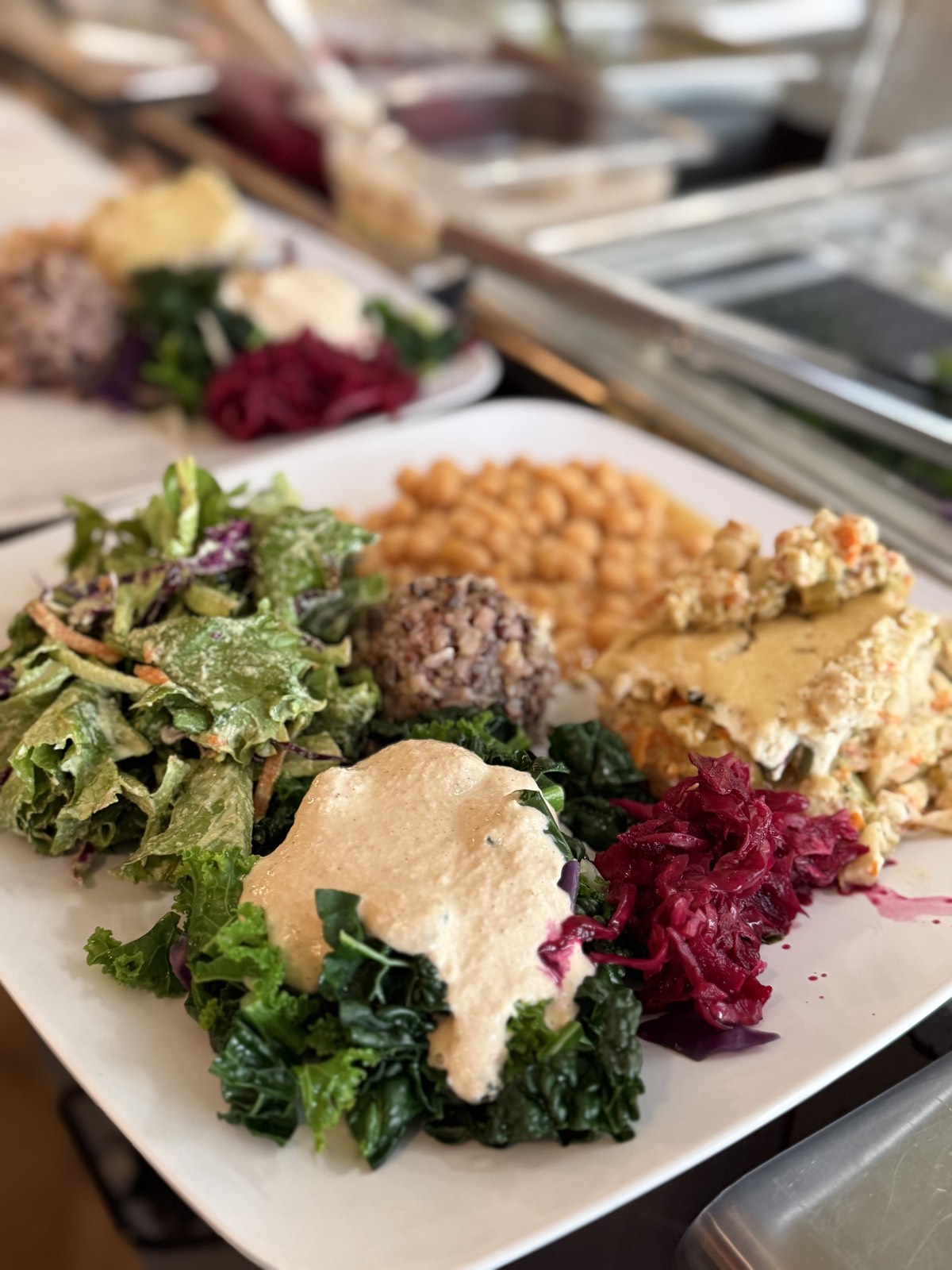 A Casa de Luz East macro plate: garden salad, chickpeas, a grain-and-bean croquette, sautéed greens with tahini sauce, a whole-food entrée, and fermented cabbage