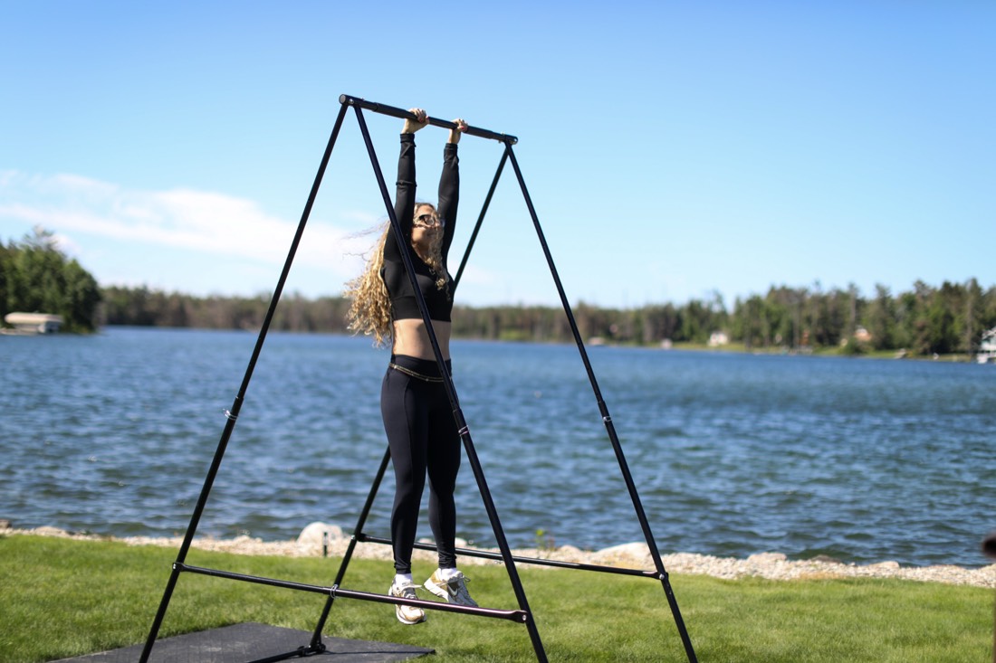 Woman competing on the pull-up bar at the 2026 Vegan Olympics, lake behind her
