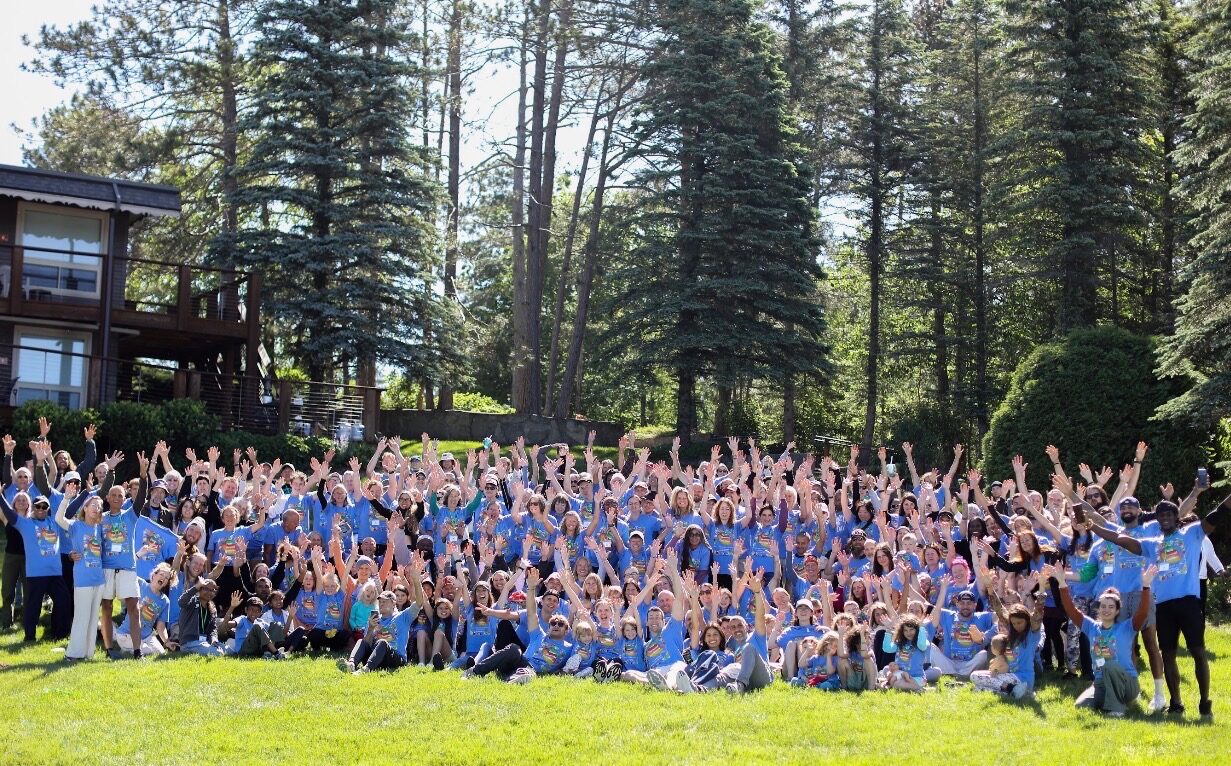 Hundreds of VWR guests of all ages in matching blue shirts, hands raised together on the lawn